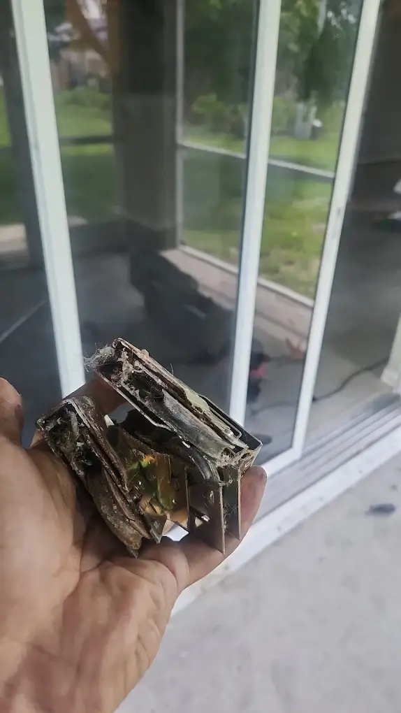 A hand holding a corroded, broken sliding door roller assembly removed from a Southwest Florida home